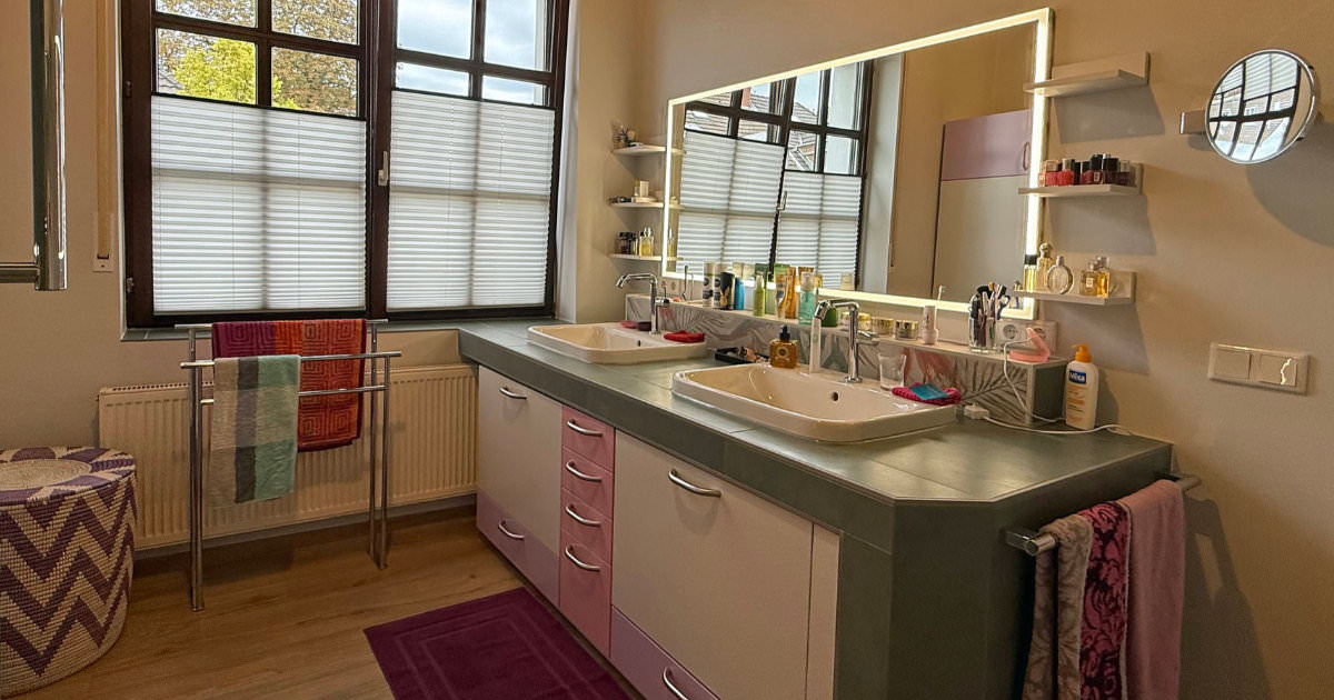 Renoviertes Badezimmer mit Doppelwaschtisch, großem, beleuchtetem Spiegelschrank, lila Akzenten und Holzboden.