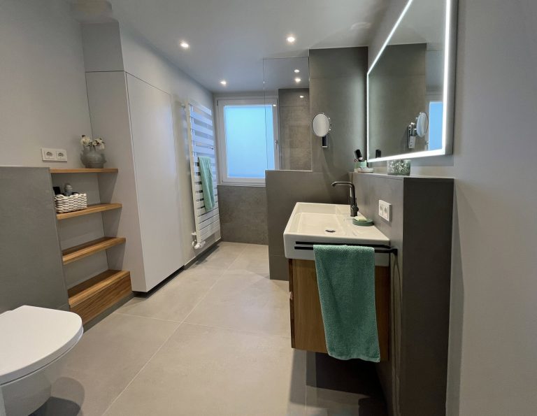 Modernes Badezimmer das von Holthausen Exklusiv in Köln renoviert wurde mit einem Waschbecken, Holzregalen, Handtuchhalter und einem großen Spiegel mit LED-Beleuchtung.