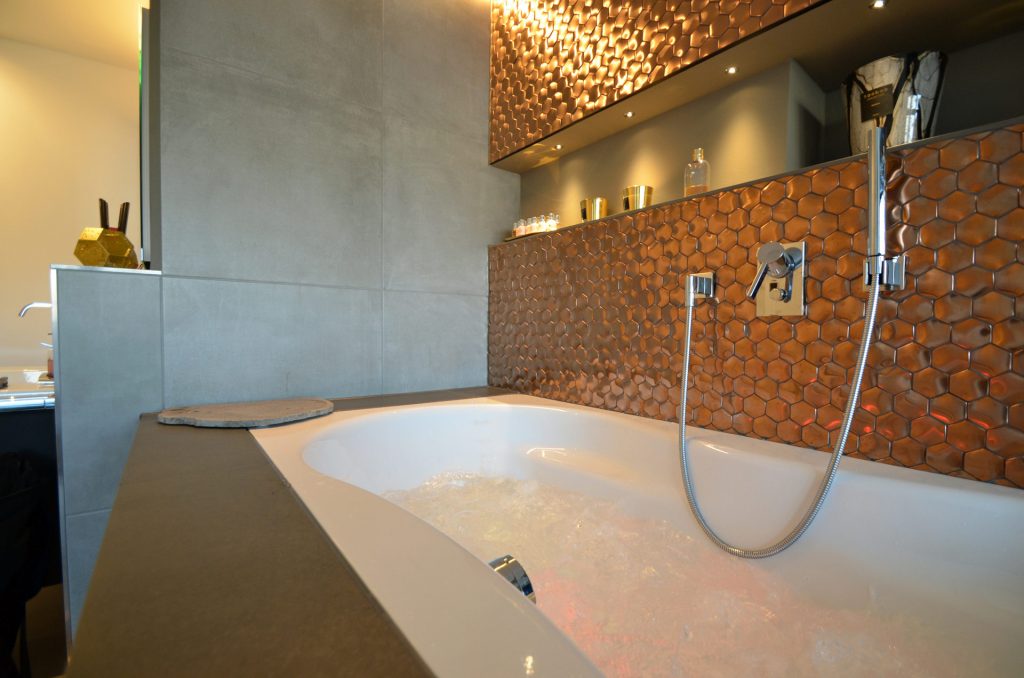 Badewanne mit einem modernen, kupferfarbenen Wandpaneel.