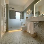 Modernes Badezimmer mit Glasdusche, Waschbecken und dekorativen Elementen in neutralen Farben.